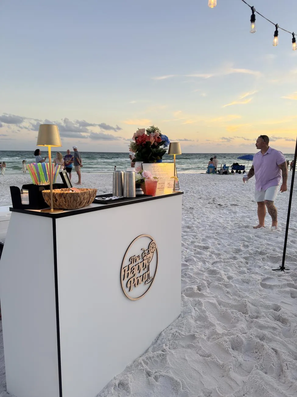 The Happy Pour bar set up on the beach at sunset with the Happy Pour sign on the front