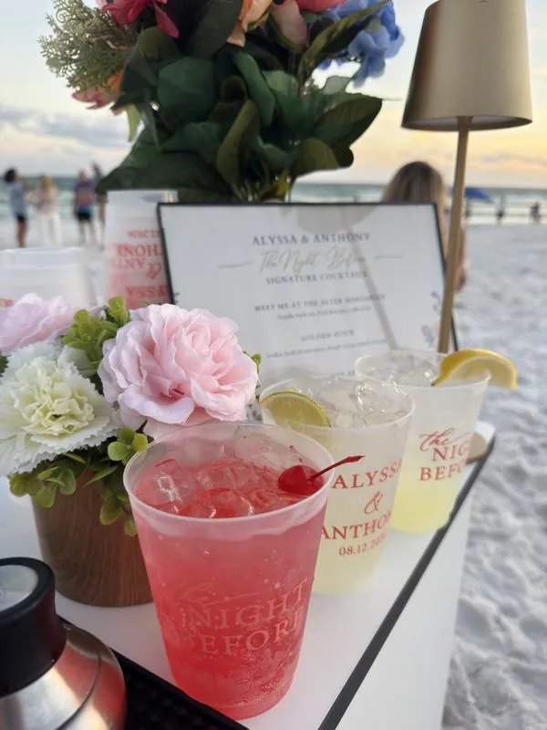 A pink signature cocktail on a beach bar with fresh flowers at sunset